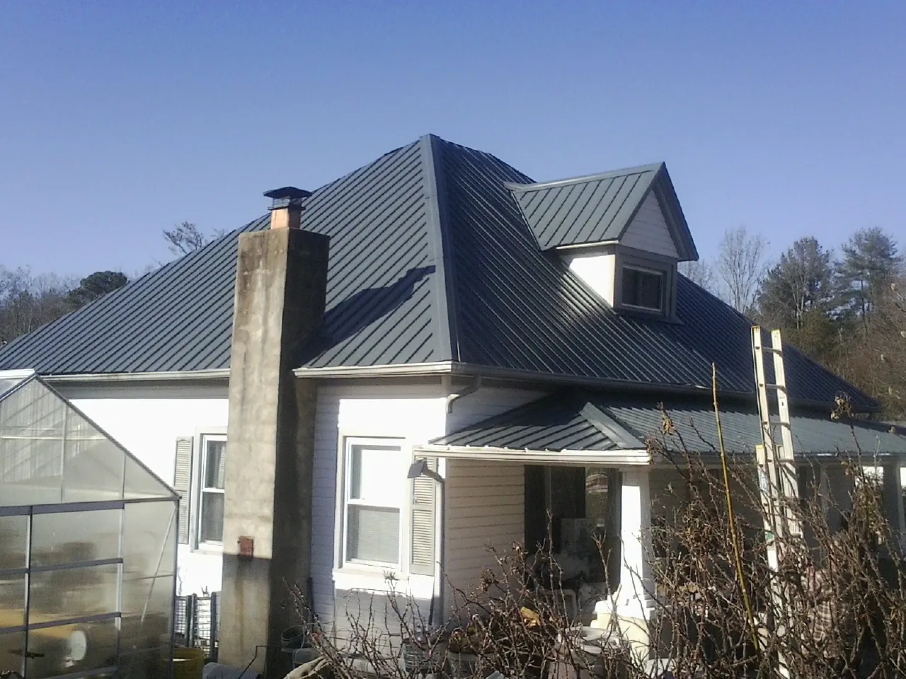 Dark blue standing seam metal roof on a white farmhouse with dormer — Slate & Tile Roof Repair by Roofing Brothers in Gilford