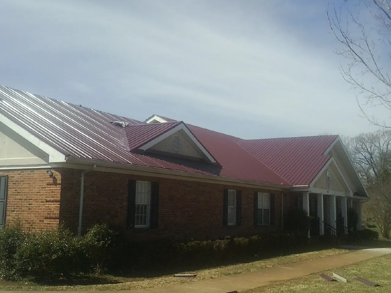 Red metal roof with gabled entries on a long brick building, from a Hail Damage Roof Repair job in Gilford