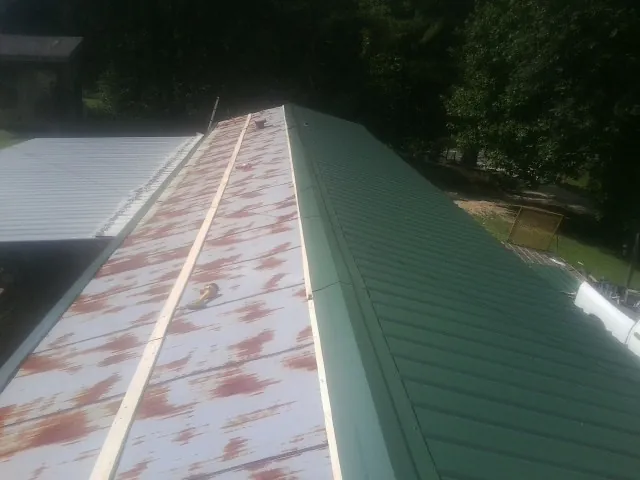 Old rusted panels beside newly installed green metal roofing — Wind Damage Roof Repair by Roofing Brothers in Gilford