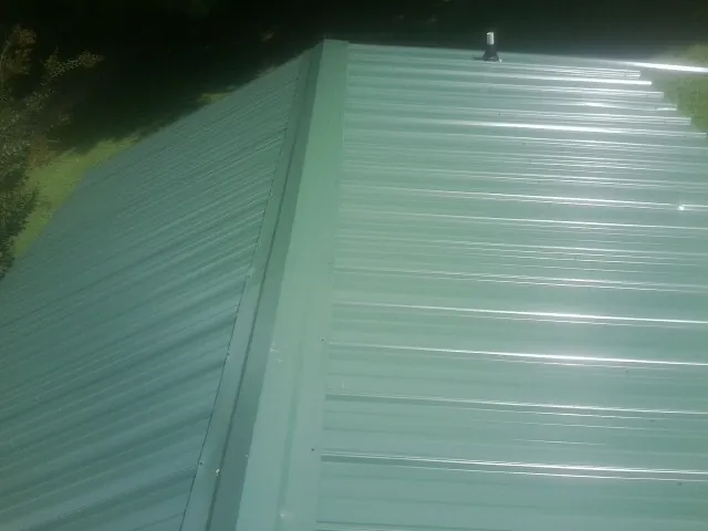 New green metal panels meeting at the ridge of a roof — Flat Roof Repair work by our crew in Gilford