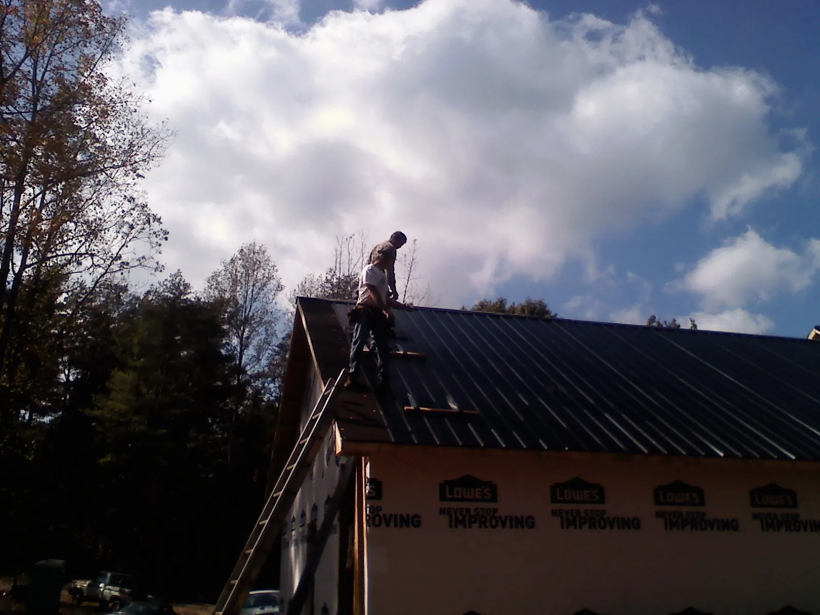 Roofer fastening dark metal panels high against a cloudy sky, from a Roof Inspection job in Gilford