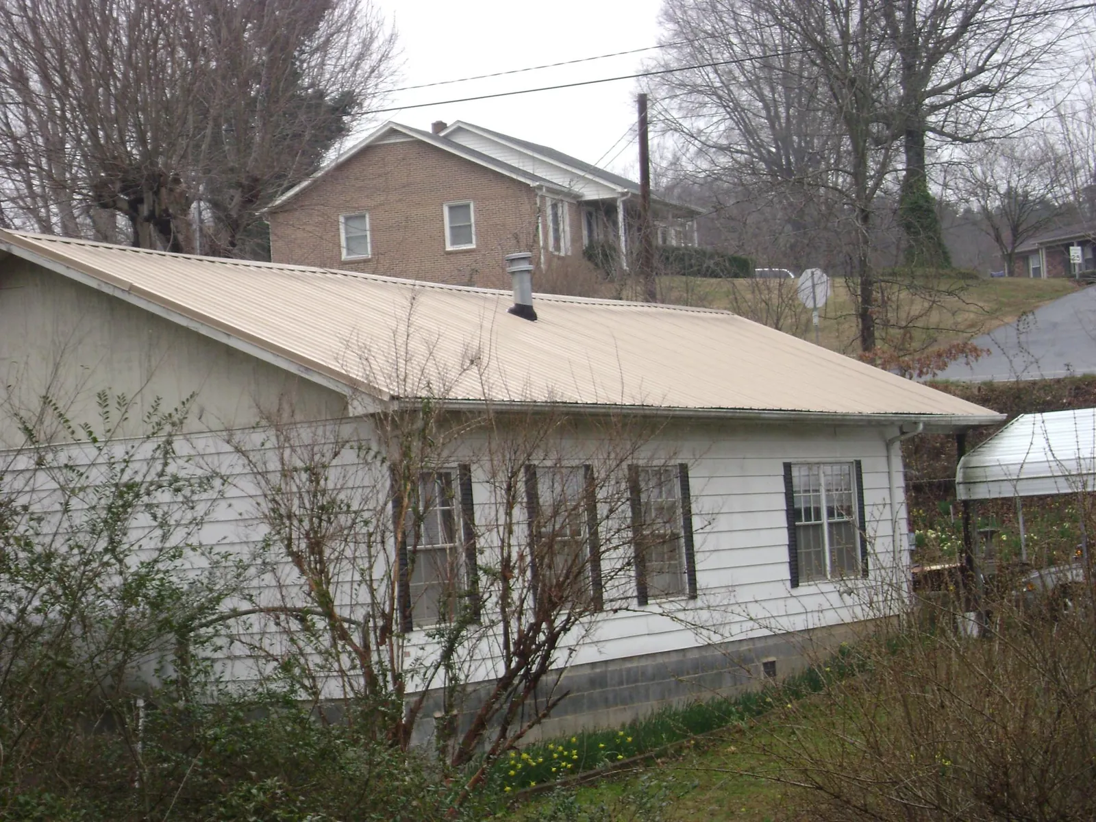 Tan metal roof on a white sided house set into a hillside — Commercial Roofing by Roofing Brothers in Gilford