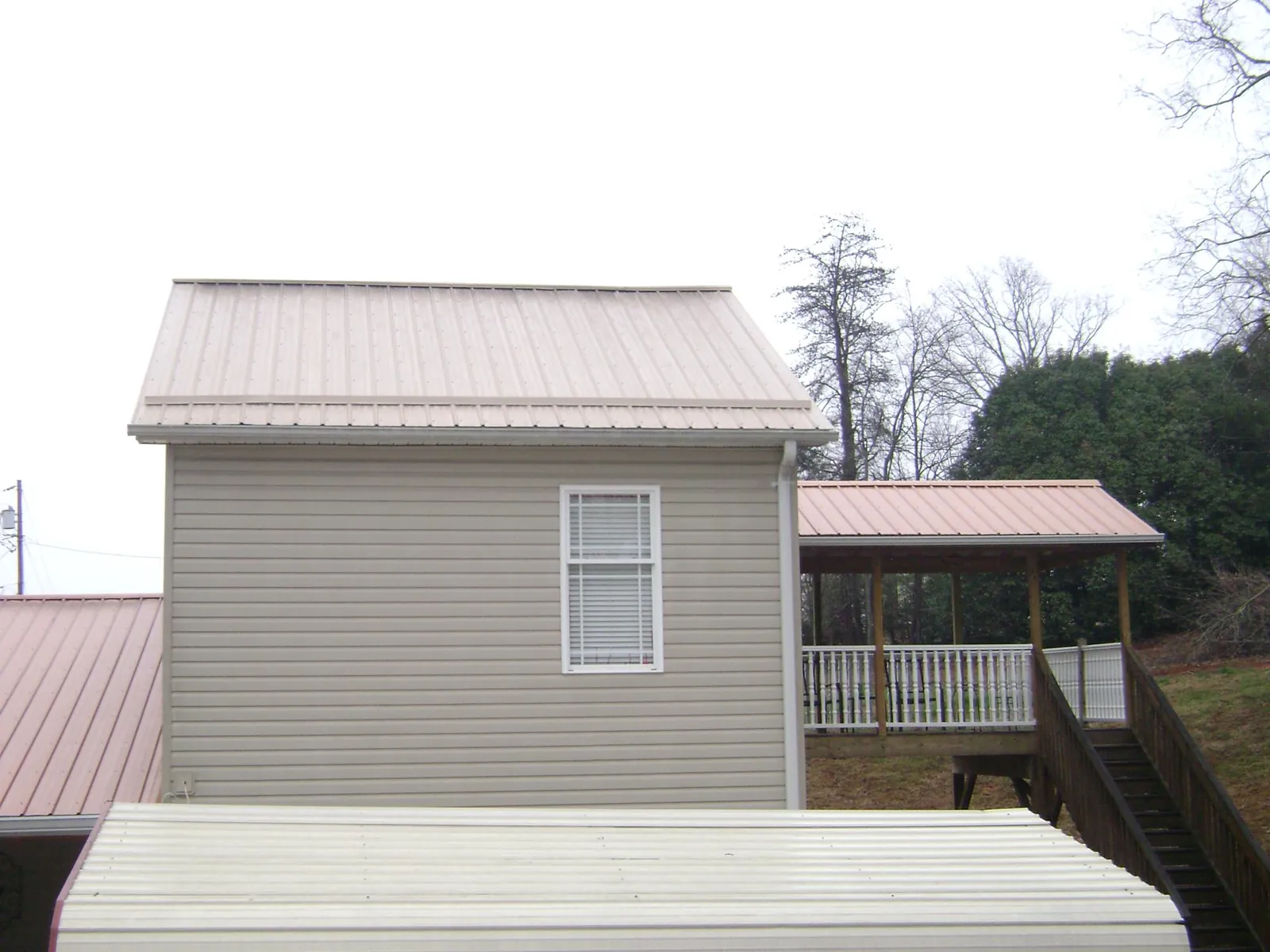 Tan metal roofs on a two story addition and attached porch, from a Roof Replacement job in Gilford